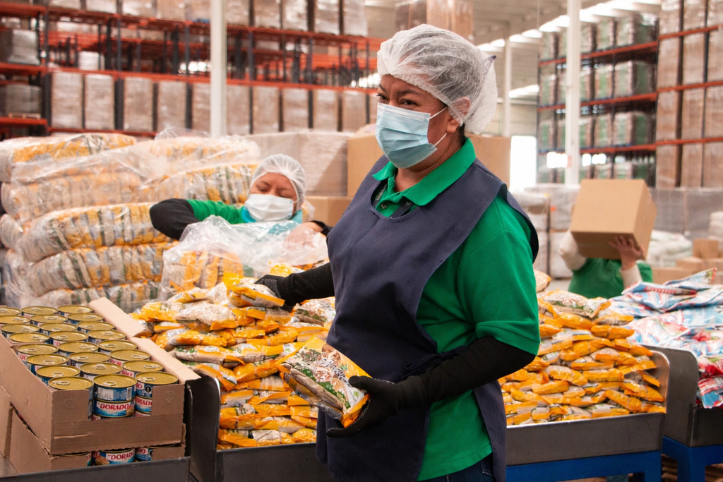 Trabajadora sostiene alimentos en planta industrial. Los dueños de Corporativo Kosmos comprenden su papel en el costo de los servicios alimentarios.